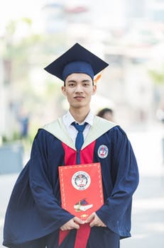 A man holding his degree, and wearing his graduation gown