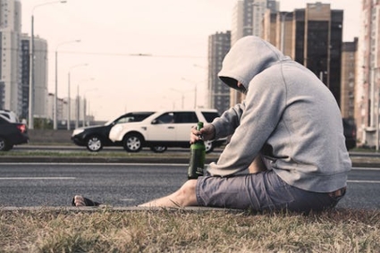 Somber scene of a man sitting alone by the roadside, holding a bottle of alcohol with a dejected posture