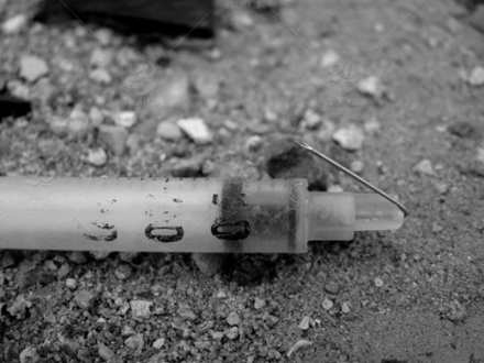 Monochrome image of a broken syringe lying on the ground
