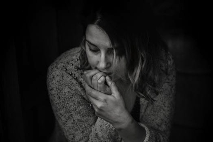 A stressed woman biting her nails, in a greyscale portrait