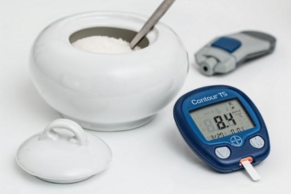 A pot of sugar placed beside a glucose meter displaying a reading of 8.4
