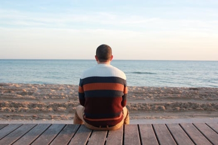 Man sitting alone by a calm riverbed, gazing into the distance