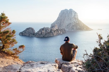 A man sits alone, gazing at a peaceful view of mountains surrounded by the sea