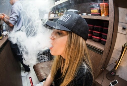 A girl exhales a thick cloud of vape smoke from her mouth