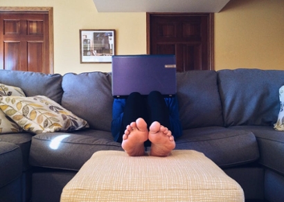 A person sits comfortably on a sofa at home, focused on working with a laptop
