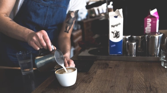 A barista pouring creamer into a coffee cup