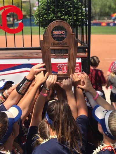 The U T A Mavericks softball team is joyfully hoisting the championship trophy above their heads together in a moment of triumph