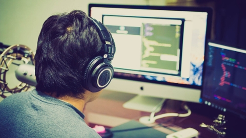 A student wearing headphones sits at a desk and works on a computer