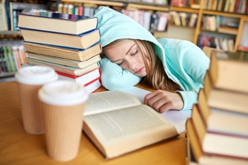 A tired student sleeping on her study table with piles of books beside her