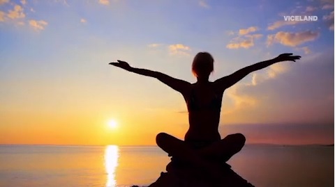 Silhouette of a woman in a seated yoga pose on a mountaintop, facing the sunrise